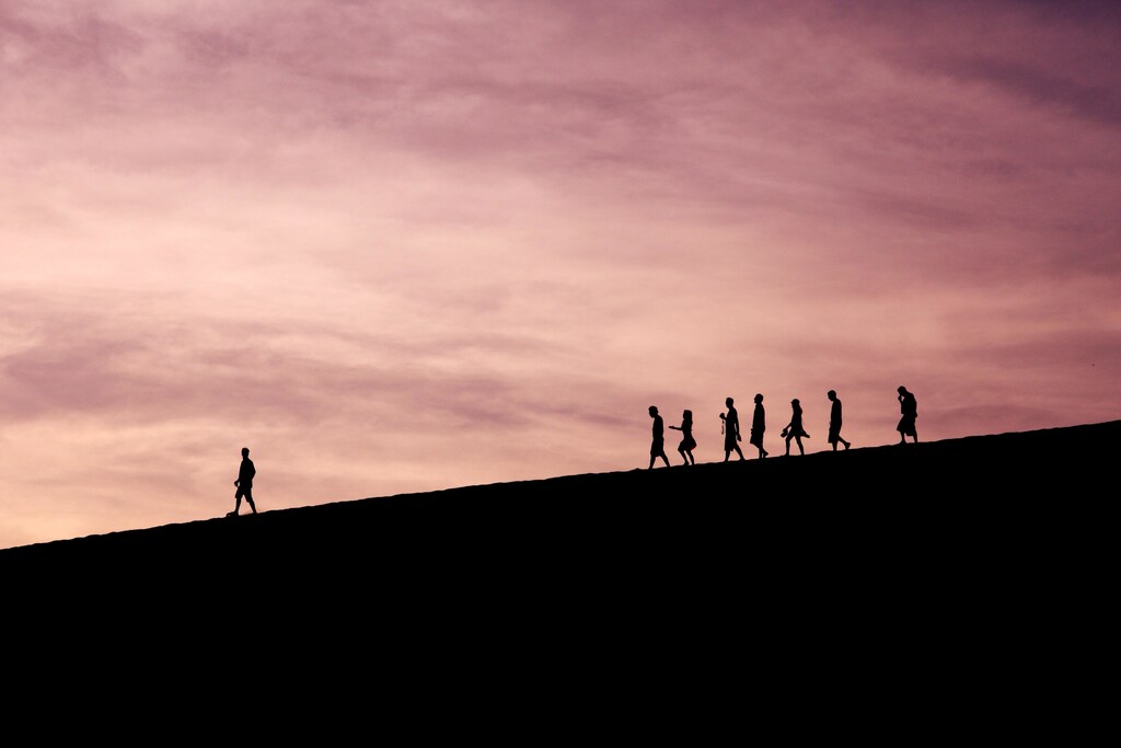 Silhouette of people walking down a hill.