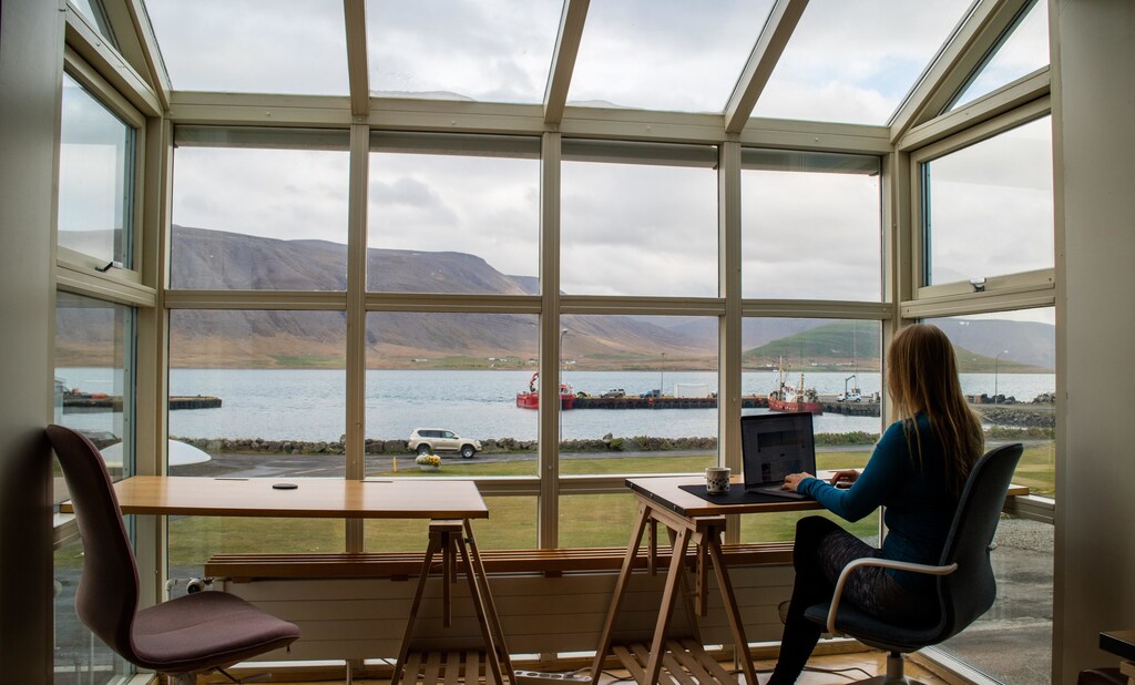 Organisations must reassess risk profiles as new work models emerge post-pandemic. Pictured; Woman working on a laptop by a window overlooking a lake and mountains.