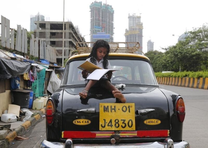 A girl studies while sitting on top of a taxi outside her shanty home at a roadside in Mumbai, India, August 11, 2015. REUTERS/Shailesh Andrade TPX IMAGES OF THE DAY - GF20000019972