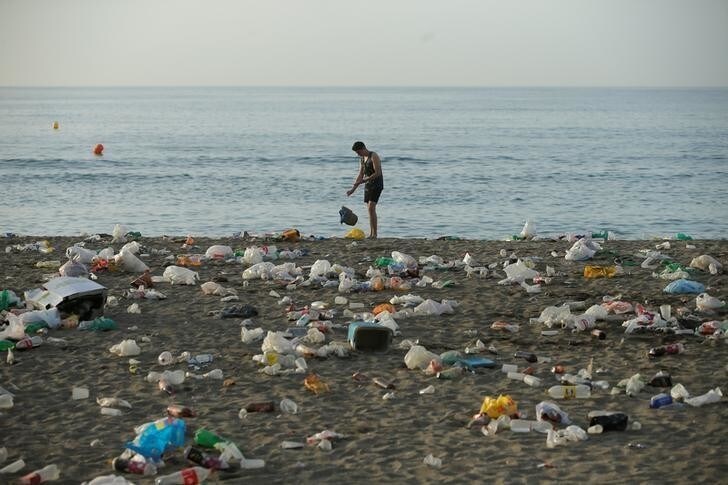 A young throws a bag surrounded by rubbish, mainly plastic bags and bottles, at dawn at Malagueta beach after celebrating the summer solstice in Malaga, Spain June 24, 2018. REUTERS/Jon Nazca
