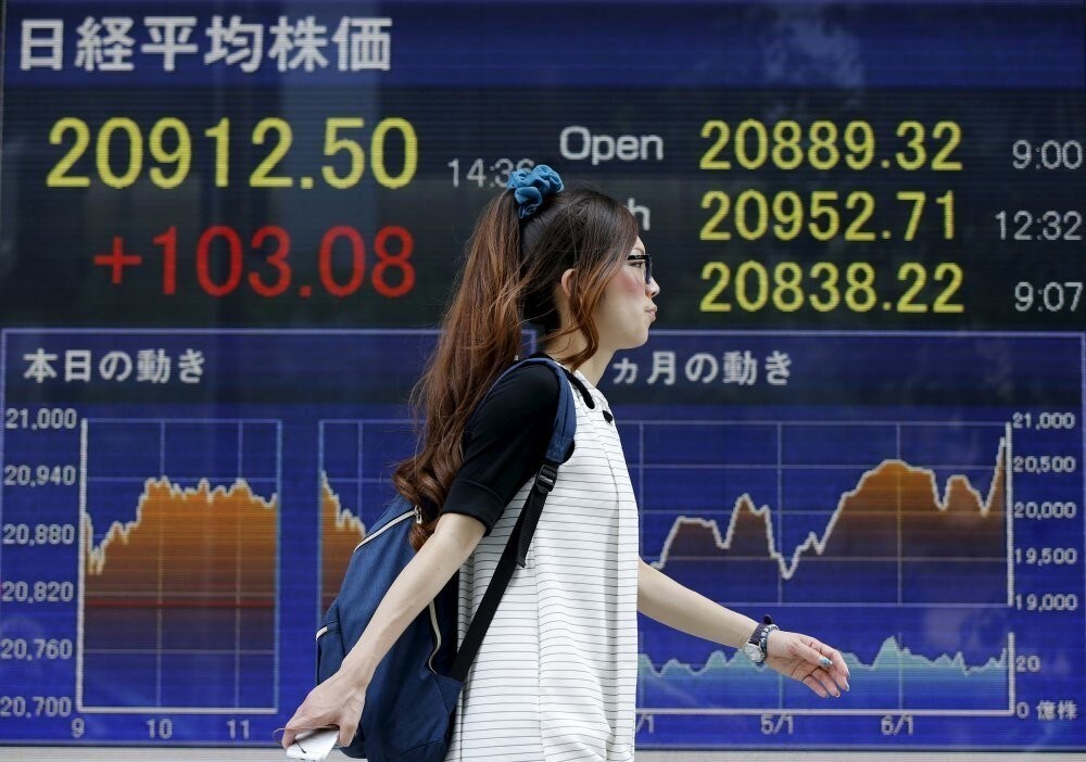 A woman walks past an electronic stock quotation board outside a brokerage in Tokyo June 24, 2015. Japan's Nikkei share average vaulted to the highest level since 1996, ramping up the gains to around 20 percent since the start of the year thanks to signs of a pick up in economic growth, earnings optimism and hopes Greece will avoid a debt default.