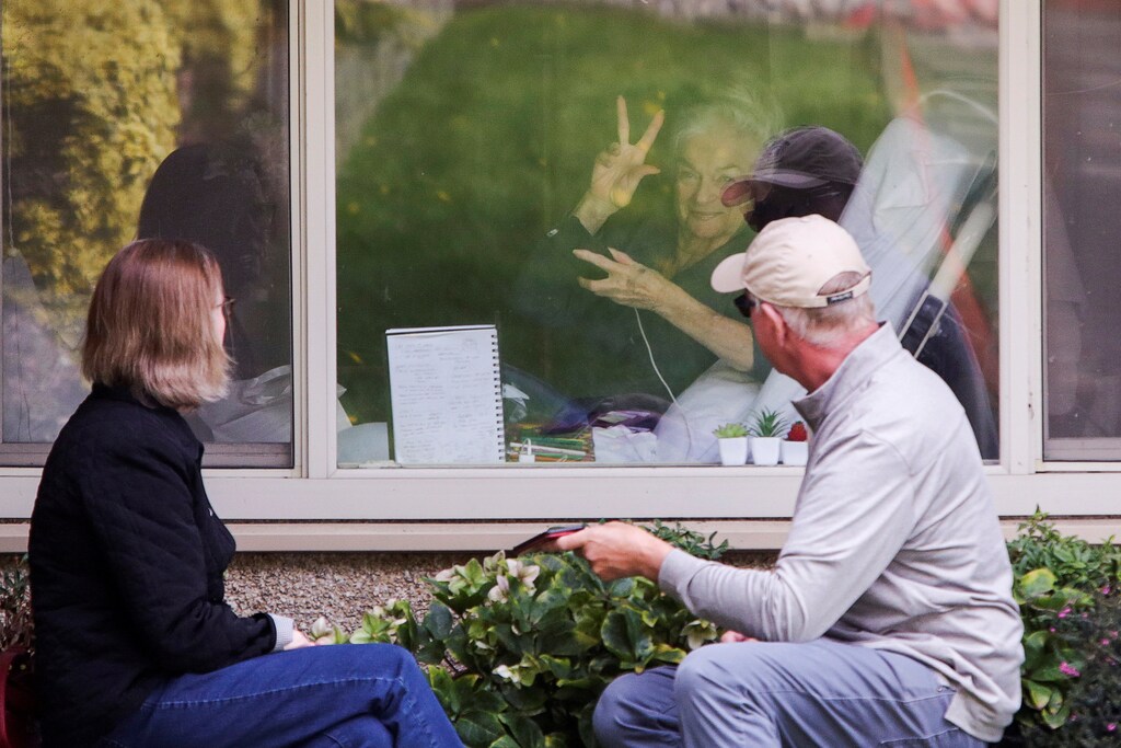 Judie Shape, 81, who tested positive for coronavirus, acknowledges press photographers gathered outside as her daughter Lori Spencer and husband Michael Spencer visit outside her room at Care Center of Kirkland, the Seattle-area nursing home which is one of the epicenters of the coronavirus (COVID-19) outbreak, in Kirkland, Washington, U.S. March 17, 2020. REUTERS/Jason Redmond - RC20MF94JE97