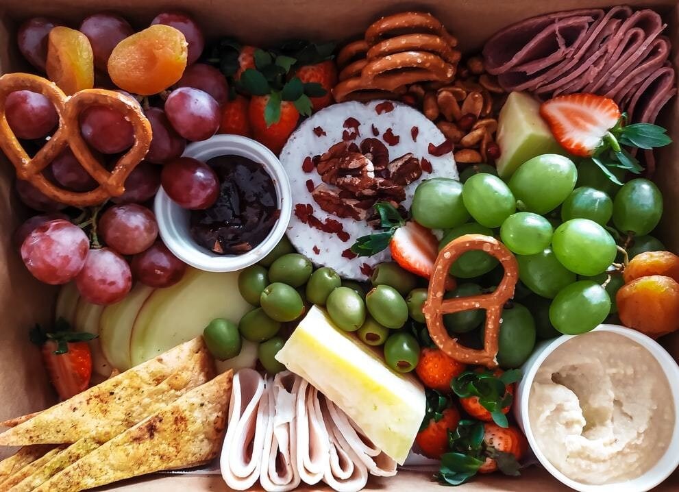 A variety of food including cheese, ham, grapes, olives, bread.