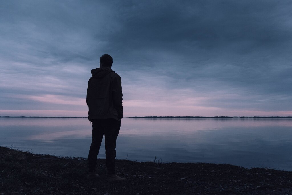 Person standing on their own, looking over a lake.