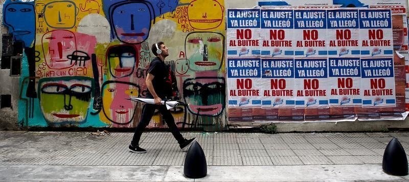 A man walks by posters (R) against payment of Argentina's defaulted debt in Buenos Aires' financial district, Argentina, March 18, 2016. The posters read "Austerity measures are already here, not to the vulture" (many Argentines deride the holdout funds as "vultures"). REUTERS/Marcos Brindicci - GF10000350804