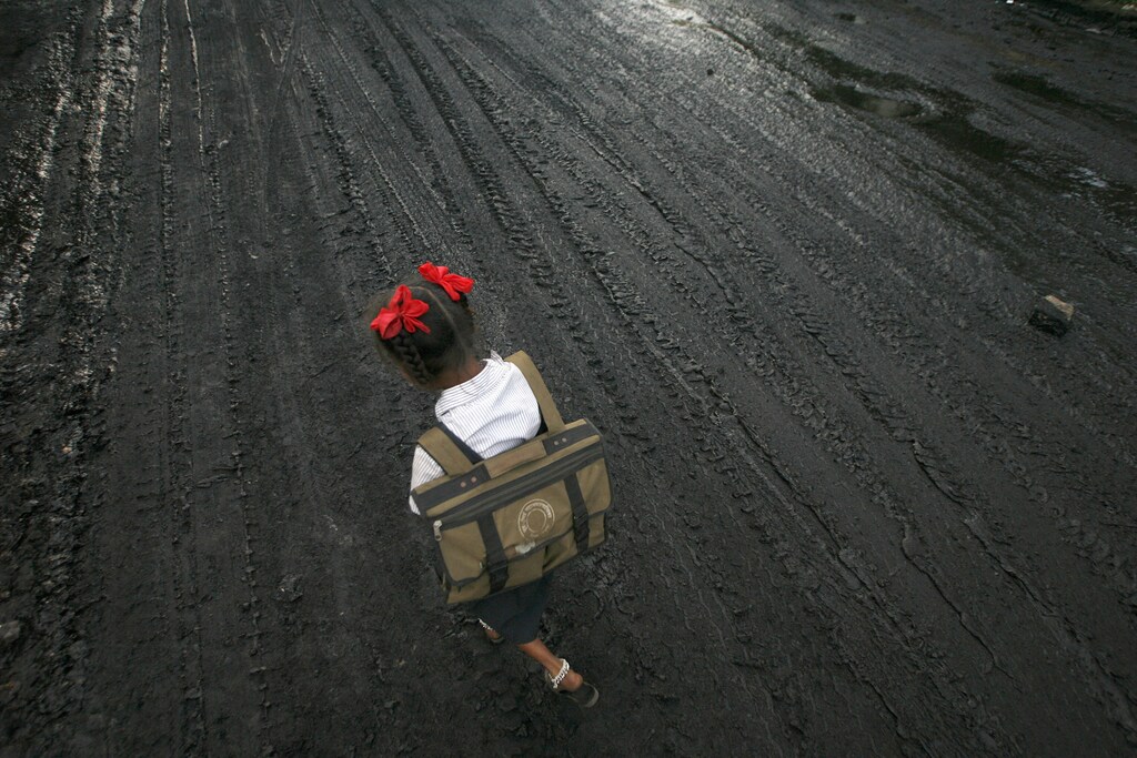 A school girl walks on a road covered with oil and soot at an industrial area in Mumbai December 3, 2009. India will not accept a legally binding emission cut nor a peak year of carbon emissions at the global climate talks in Copenhagen, Environment Minister Jairam Ramesh said on Thursday. REUTERS/Arko Datta (INDIA ENVIRONMENT SOCIETY BUSINESS) - RTXRERY