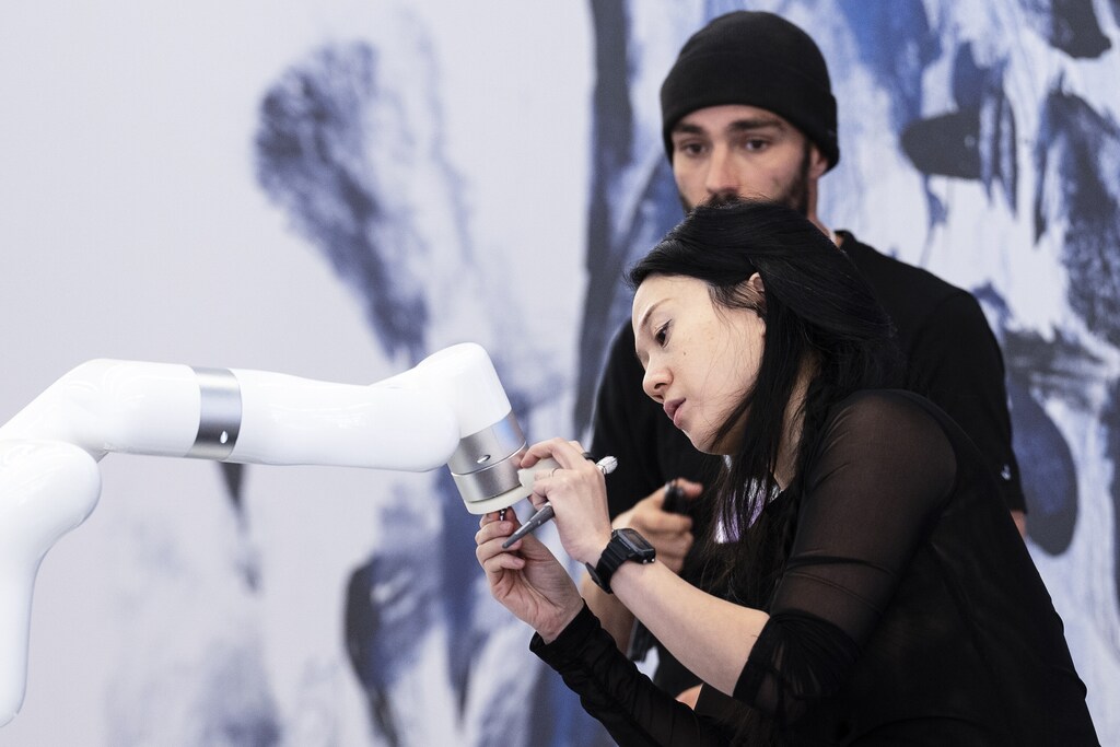 A woman inspects a robotic arm, and a man stands in the background, in a picture taken from the World Economic Forum Annual Meeting 2025 in Davos-Klosters, Switzerland