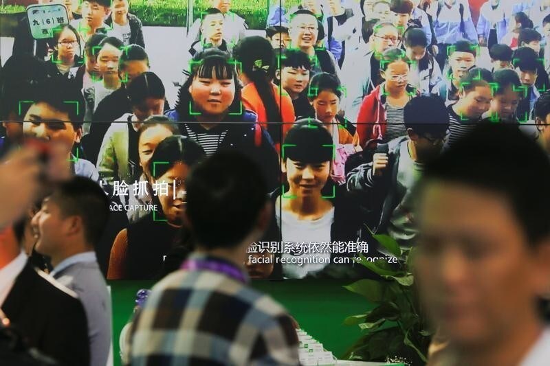 Visitors walk past a screen showing a demonstration of facial recognition software at the Security China 2018 exhibition on public safety and security in Beijing, China October 23, 2018. Picture taken October 23, 2018. REUTERS/Thomas Peter - RC1D51E07770