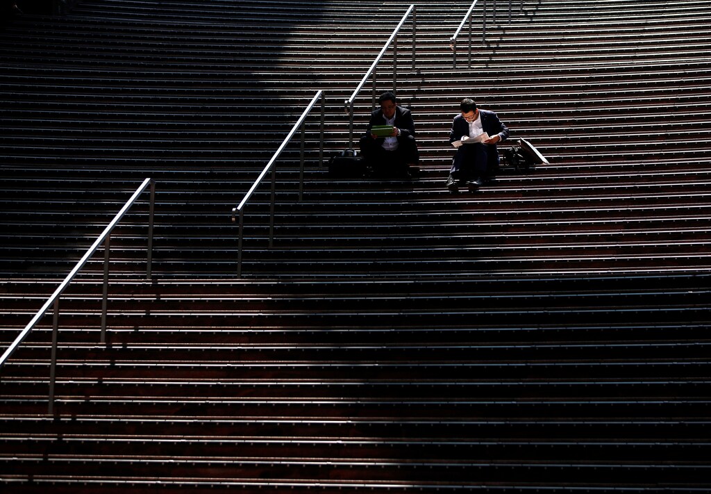 Businessmen using tablet computers sit on steps at Kyoto station in Kyoto, Japan May 11, 2017. REUTERS/Issei Kato - RTS164WE