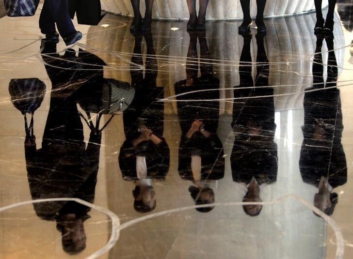 A porter carries luggage past a group of reception staff that are reflected in the floor as they stand in the foyer of the five-star rated Sofitel Hotel in Beijing November 19, 2007. City tourism officials and Olympics organizers are confident Beijing's 700-plus star-rated hotels can absorb the onslaught of half a million foreign and domestic visitors expected each day for 17 days beginning August 8, 2008. REUTERS/David Gray (CHINA)
