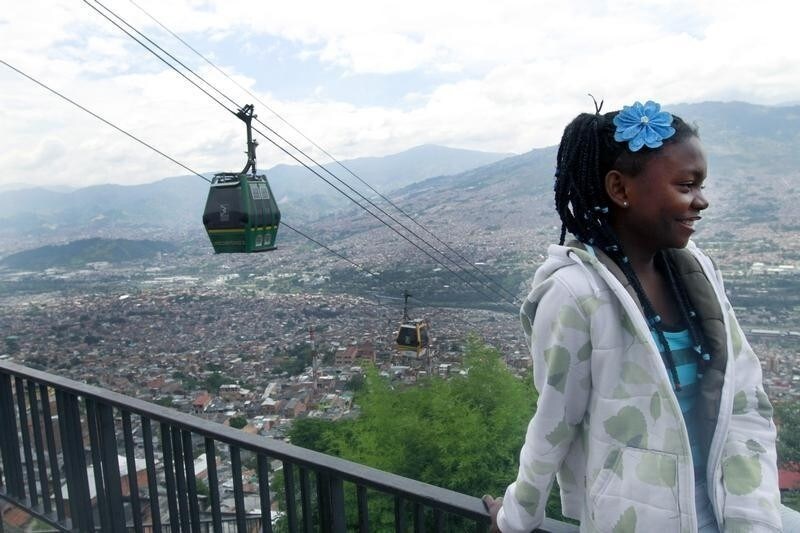 A girl stands nearby as cable cars pass behind her, at a viewpoint overlooking Medellin March 1, 2013.