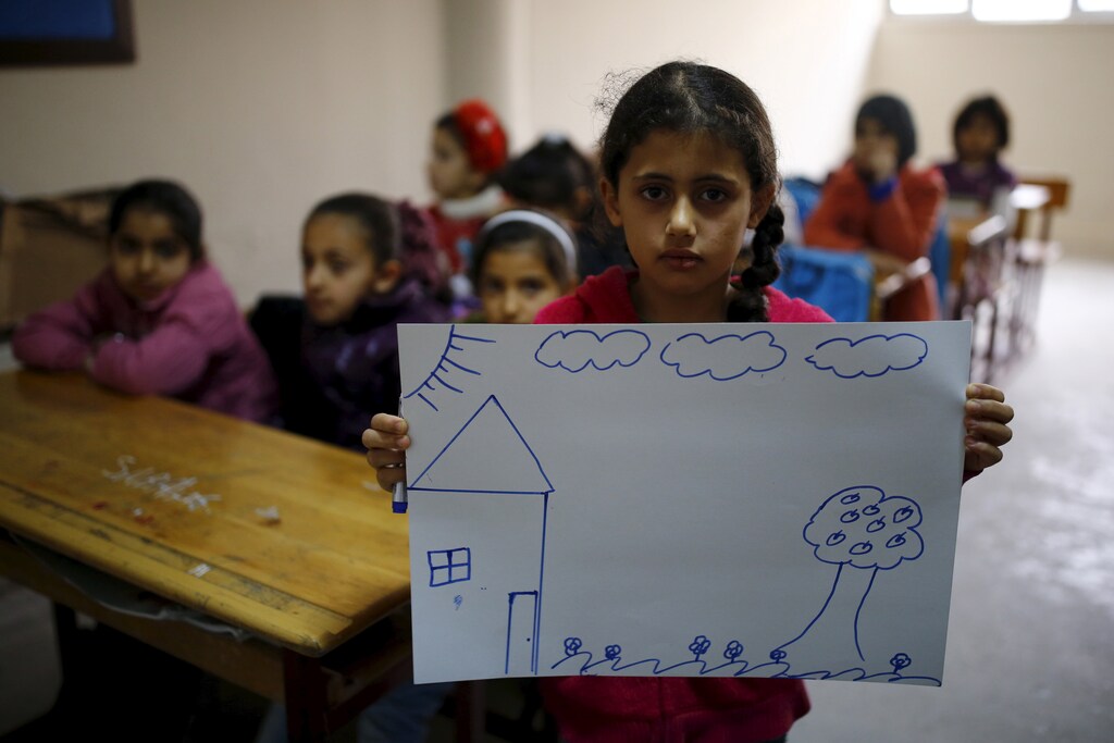 Syrian refugee girl Nur El-Huda, 9, shows a drawing of her home in Syria, in her classroom in Yayladagi refugee camp in Hatay province near the Turkish-Syrian border, Turkey, December 16, 2015.