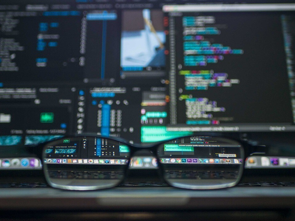 A pair of glasses in front of multiple computer screens