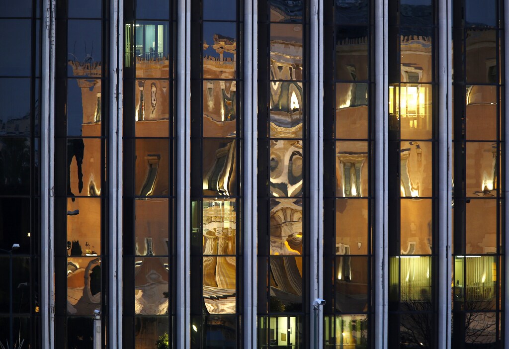 A man talks on the phone in his office (top L) at Greece's Ministry of Foreign Affairs as the Greek parliament is reflected on the building in Athens March 12, 2015. Greece has promised its lenders to reform its state sector, to implement labour reforms, such as opening up closed professions, to make its economy more competitive, improve its tax administration and fight tax evasion and corruption, which have been widely blamed for the debt crisis. REUTERS/Yannis Behrakis (GREECE - Tags: POLITICS BUSINESS) - RTR4T4H1