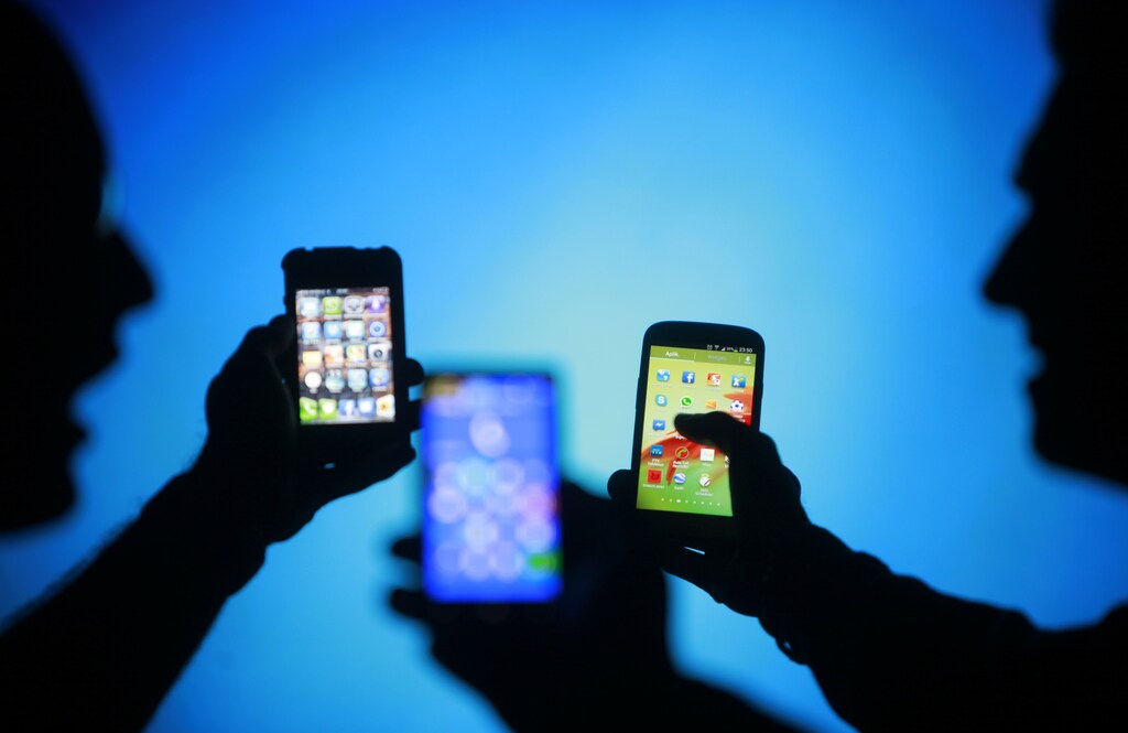 Men are silhouetted against a video screen as they pose with Samsung Galaxy S3, Nokia Lumia 820 and iPhone 4 smartphones (R-L) in this photo illustration taken in the central Bosnian town of Zenica, May 17, 2013.