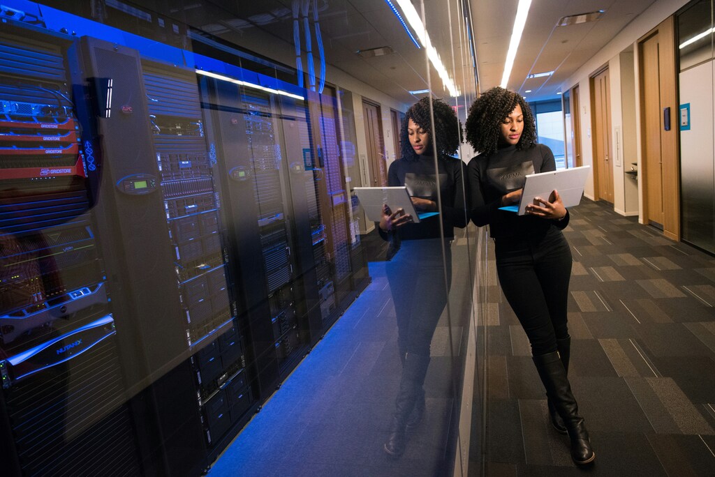 A woman is on her laptop next to a server room: To bridge the cybersecurity gap, leaders must address it as a governance issue