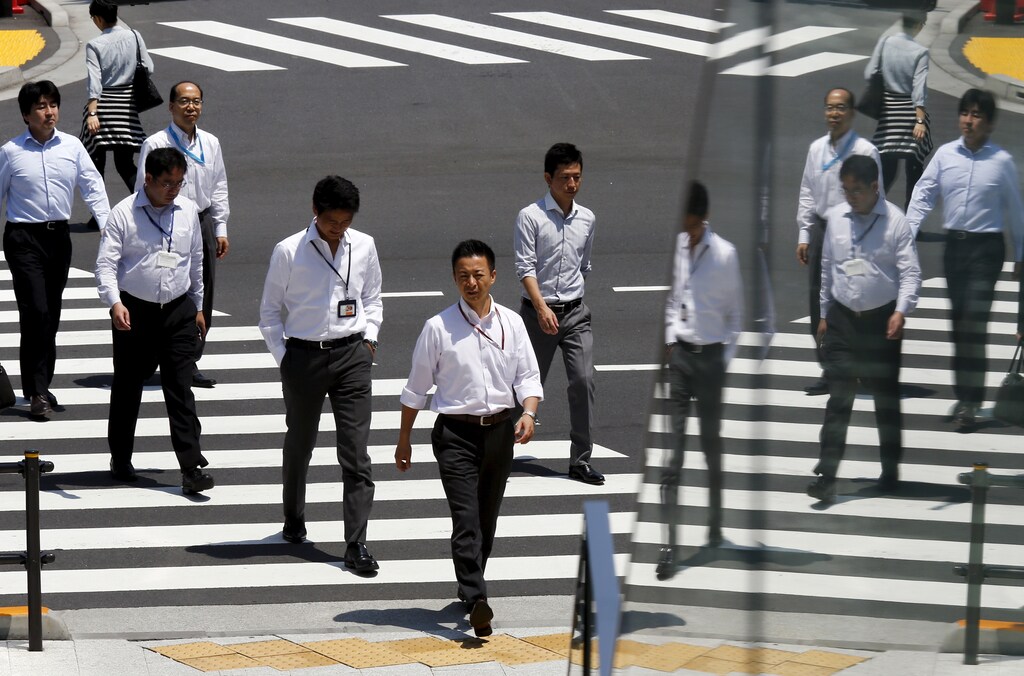 Office workers are reflected in a glass railing as they cross a street during lunch hour in Tokyo June 1, 2015. REUTERS/Thomas Peter