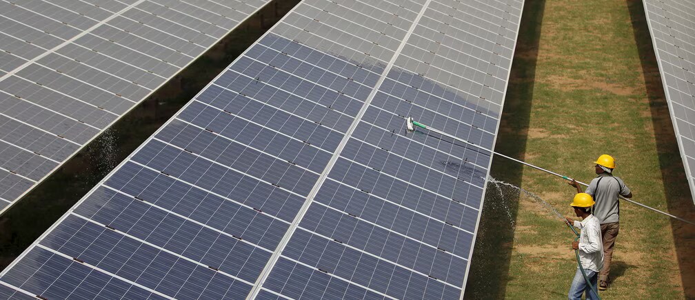 Workers hose down solar panels on a solar farm.