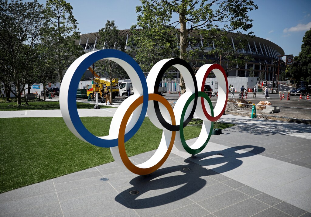 Construction workers and passersby are seen through Olympic rings in front of the construction site of the New National Stadium, the main stadium of Tokyo 2020 Olympics and Paralympics, in Tokyo, Japan June 13, 2019. REUTERS/Issei Kato - RC18D27C1C80