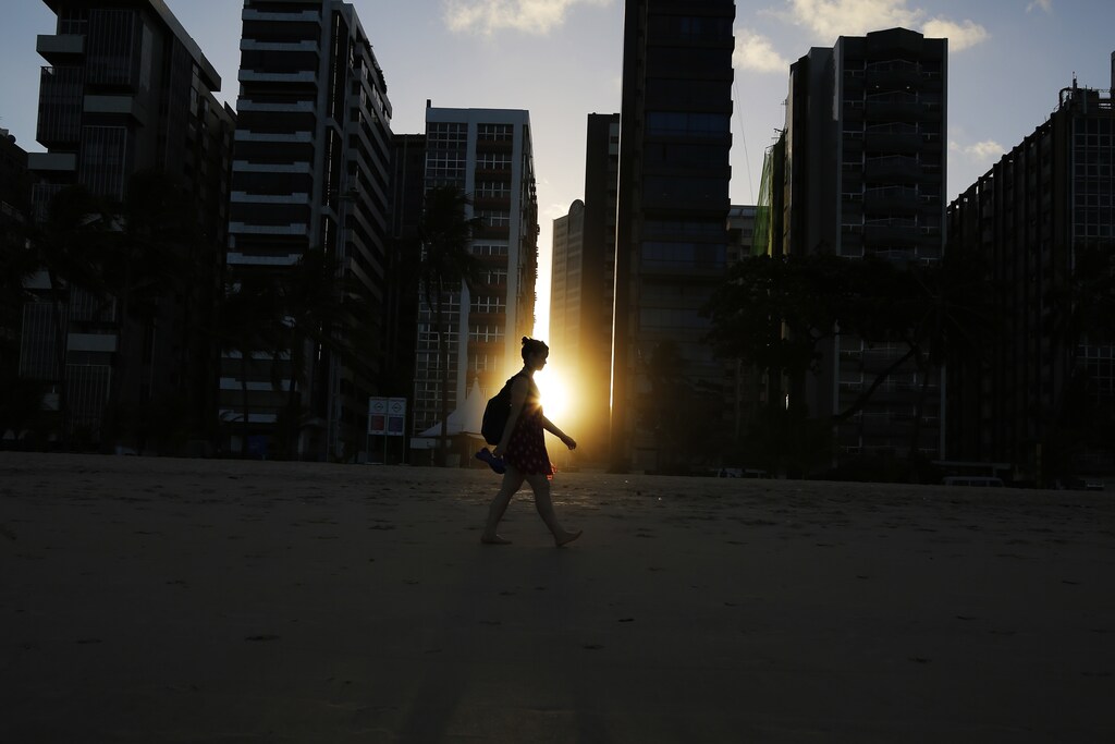 A woman walks on the beach as the sun sets between buildings in Recife June 10, 2014. In a project called 'OnThe Sidelines' Reuters photographers share pictures showing their own quirky and creative view of the 2014 World Cup in Brazil. REUTERS/Brian Snyder (BRAZIL) - RTR3T4DN