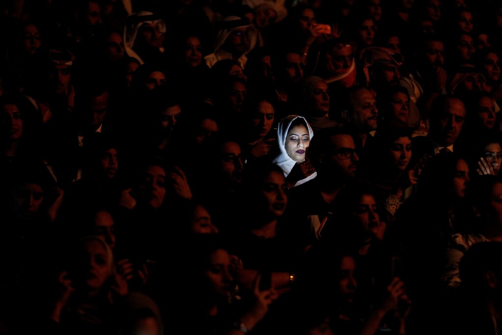 Light from a mobile phone illuminates a woman's face at a concert in Bahrain
