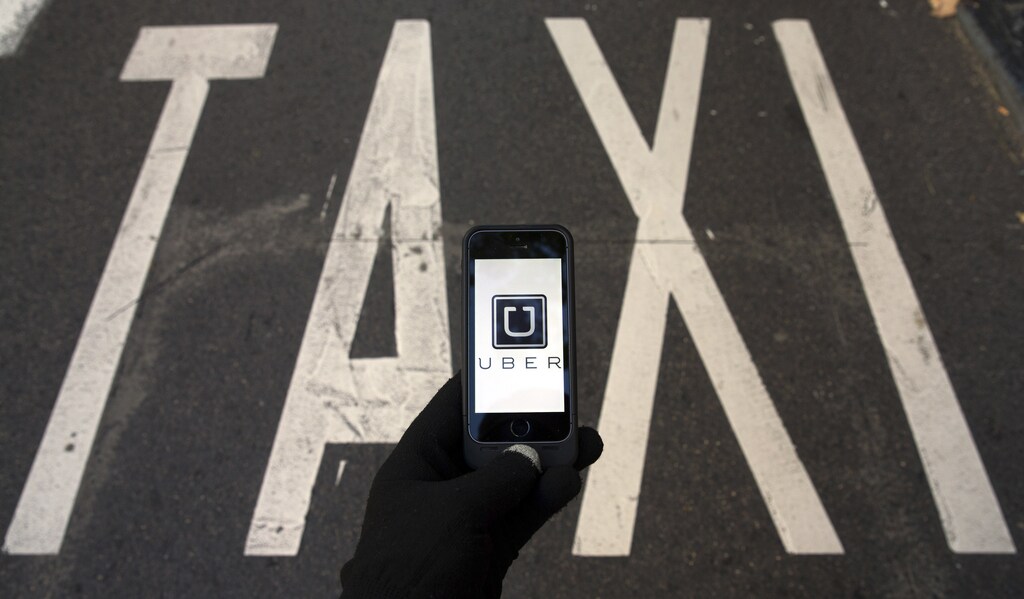 The logo of car-sharing service app Uber on a smartphone over a reserved lane for taxis