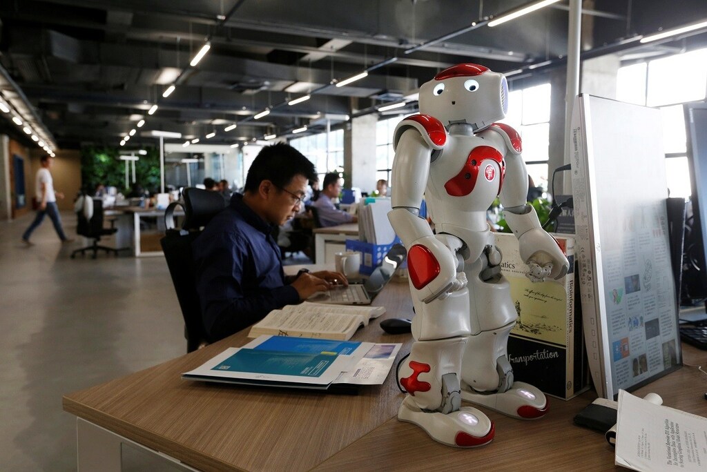 Staff work behind a robot at iCarbonX, a start up company focusing on combining genomics with other health factors to create a digitalized form of life, in Shenzhen, China May 25, 2018. REUTERS/Bobby Yip - RC13C9C08470