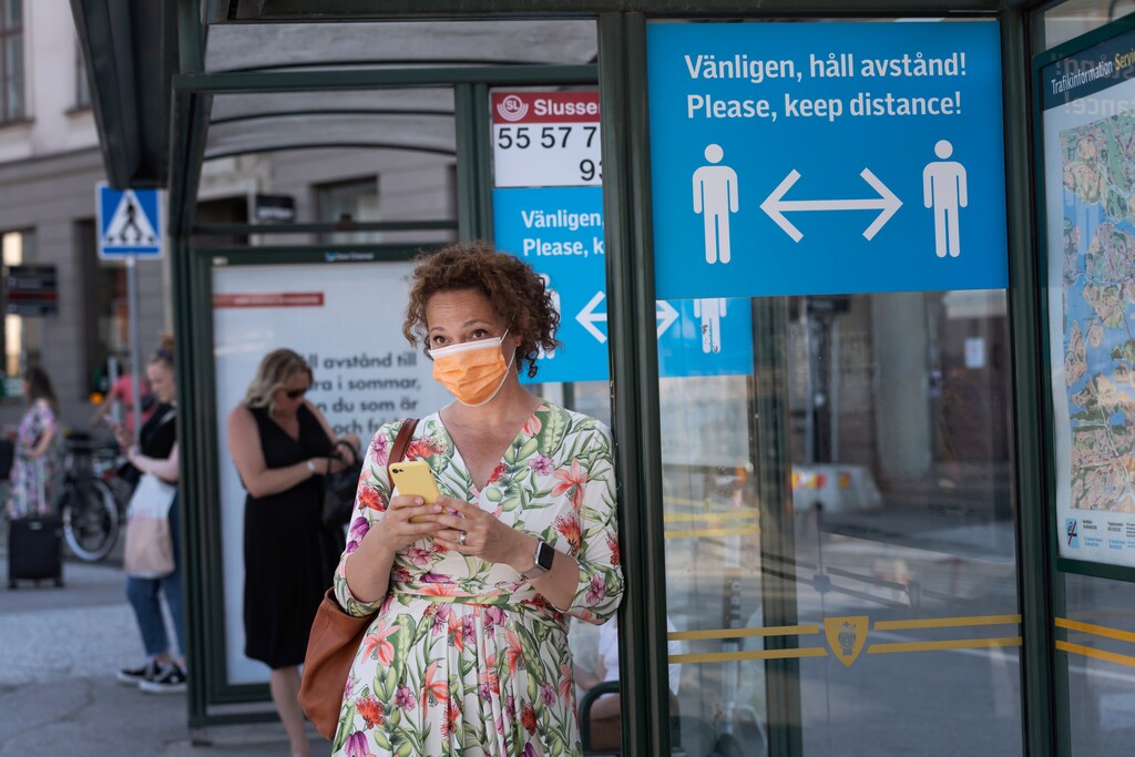A woman wearing a face mask is seen in a bus stop next to an information sign asking people to keep social distance due to the outbreak of coronavirus disease (COVID-19), in Stockholm, Sweden June 26, 2020. Stina Stjernkvist/ TT News Agency/via REUTERS ATTENTION EDITORS - THIS IMAGE WAS PROVIDED BY A THIRD PARTY. SWEDEN OUT. NO COMMERCIAL OR EDITORIAL SALES IN SWEDEN. - RC25HH9OZYTC