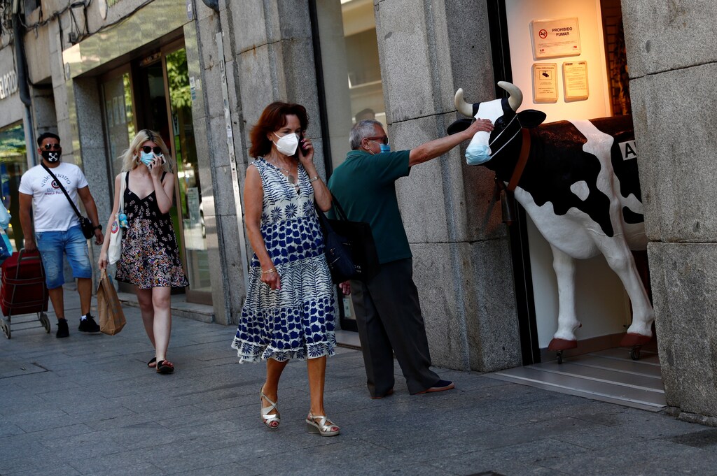 A man touches the face of a figure of a cow wearing a protective mask outside a store, amid the coronavirus disease (COVID-19) outbreak, in Madrid, Spain, June 30, 2020. REUTERS/Susana Vera - RC2NJH9PVS1N