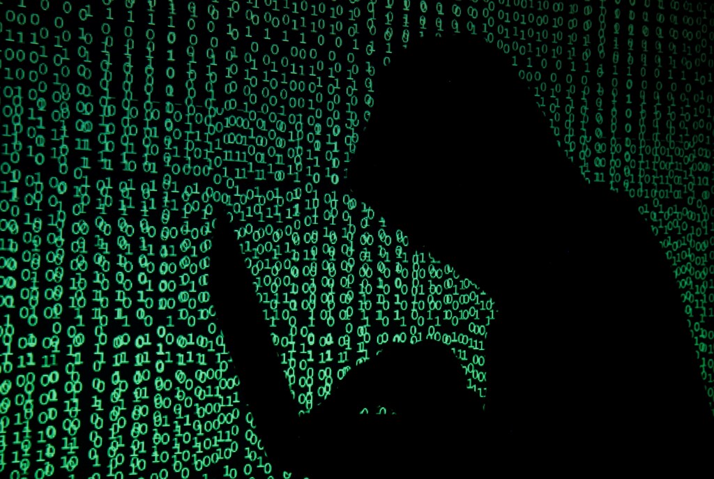 A hooded man holds a laptop computer as cyber code is projected on him in this illustration picture taken on May 13, 2017. Capitalizing on spying tools believed to have been developed by the U.S. National Security Agency, hackers staged a cyber assault with a self-spreading malware that has infected tens of thousands of computers in nearly 100 countries. REUTERS/Kacper Pempel/Illustration - RTX35ORW