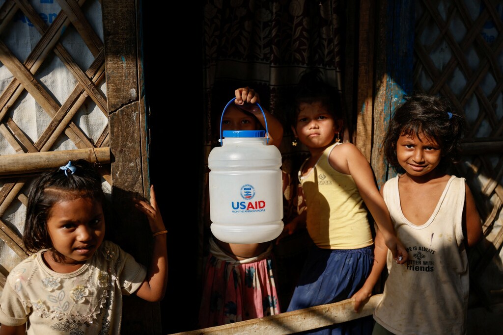 A Rohingya refugee girl holds a jar with USAID logo imprinted, at the refugee camp in Cox's Bazar, Bangladesh, March 16, 2025. Global aid cuts threaten youth development.