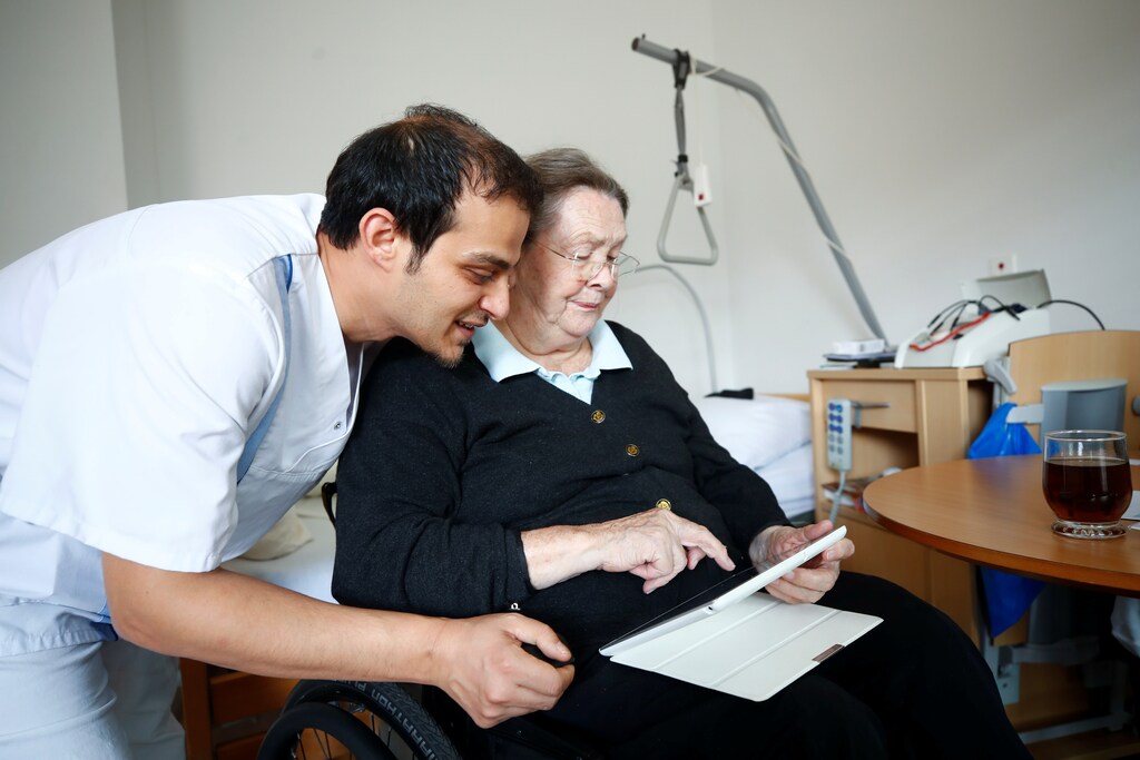 Elisabeth Grohmann, an 85-year-old former sports teacher and Amer Kabara, a 35-year-old former refugee from Syria watch a funny movie about Germany's anti-refugee party Alternative fuer Deutchland AFD on Grohmann's tablet at an old people's home in Duesseldorf, Germany, September 12, 2018. Picture taken September 12, 2018. Kabara, who fled to Germany from the civil war-torn Syrian capital of Damascus is on an 18-month educational project called "Care for Integration" to become a state-approved nurse for the elderly in Germany. REUTERS/Wolfgang Rattay - RC1D5ED12810