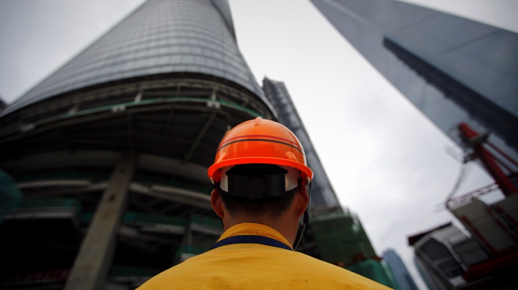 A construction worker stand at the base of the Shanghai Tower (L), which is under construction, at the financial district of Pudong in Shanghai August 2, 2013.