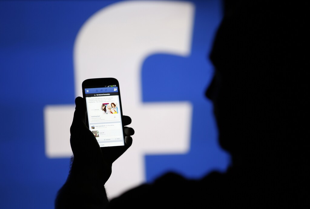 A man is silhouetted against a video screen with an Facebook logo as he poses with an Samsung S4 smartphone in this photo illustration taken in the central Bosnian town of Zenica, August 14, 2013. REUTERS/Dado Ruvic/File Photo - RTX2IVBO
