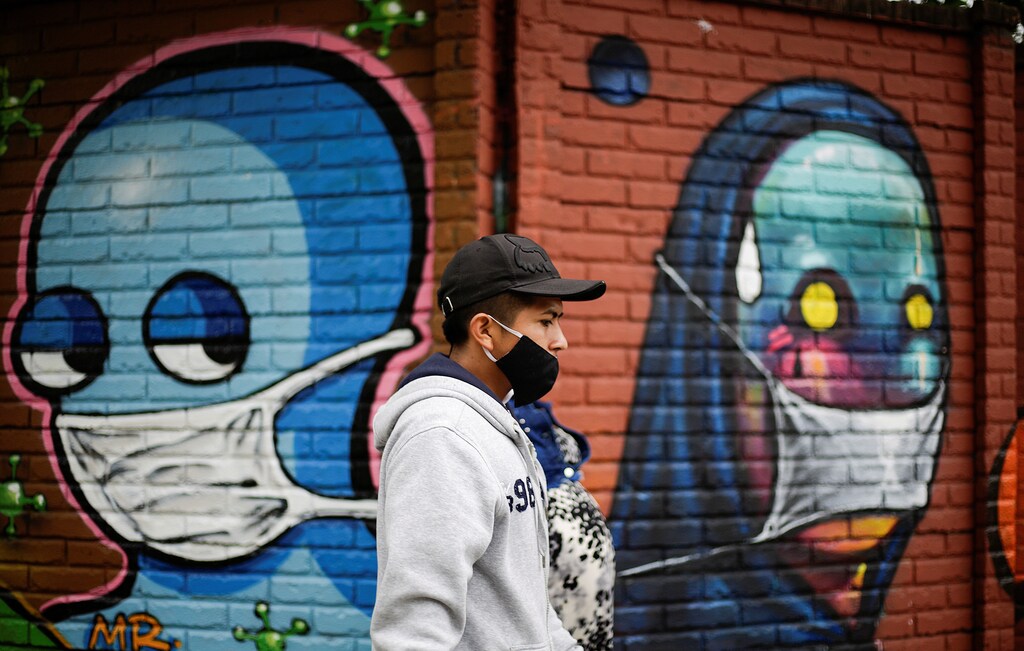 Un hombre con una mascarilla facial camina junto a una pared con graffitis después de que las autoridades sanitarias revocan las medidas de reapertura tras el aumento de los casos de la enfermedad coronavirus (COVID-19) en San José (Costa Rica) el 13 de julio de 2020.