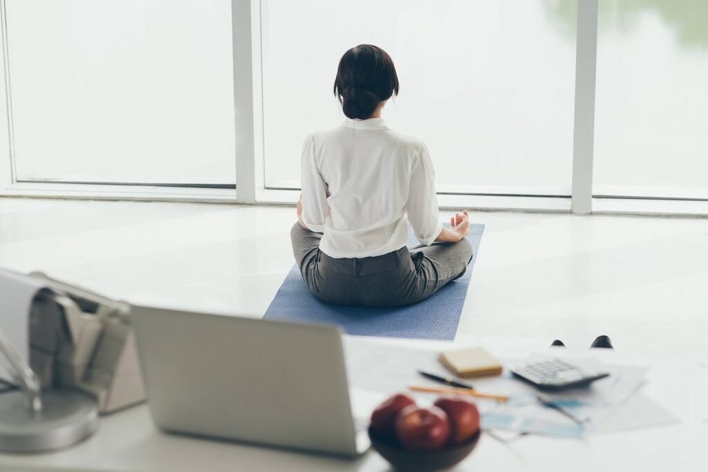 Office worker meditating on the floor, rear view; workplace culture