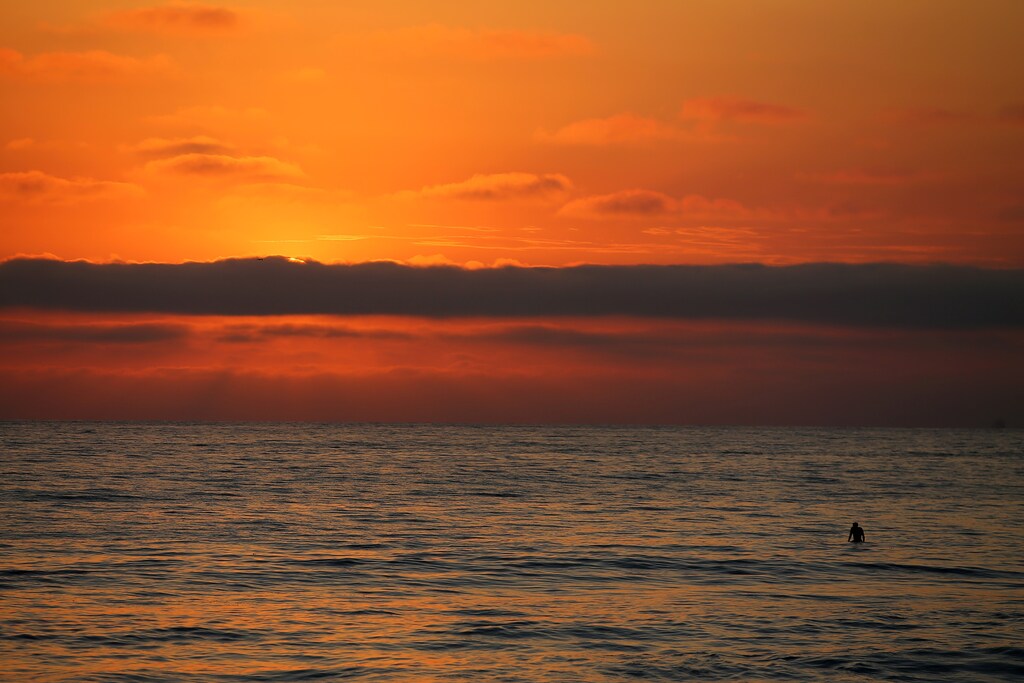 A lone surfer watches the sun set behind a cloud off the beach in Encinitas, California, U.S., July 5, 2017. REUTERS/Mike Blake - RTX3A831