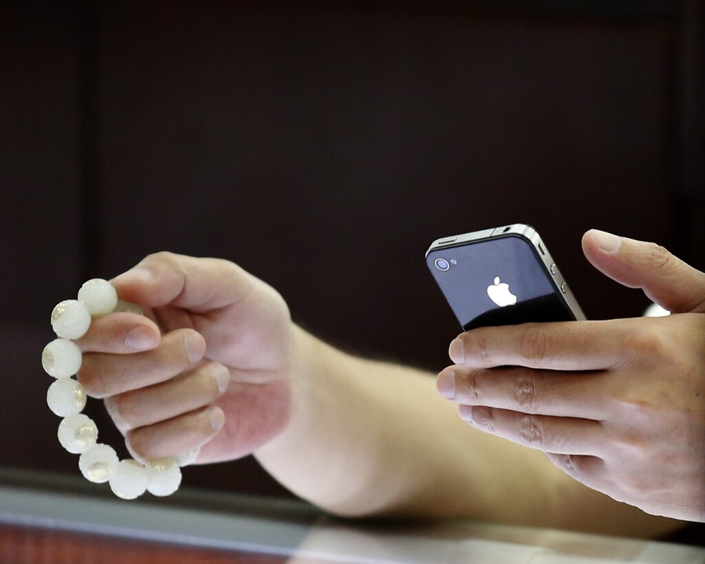 A man uses Apple's iPhone as he holds prayer beads at an antique shop in Beijing July 31, 2013.