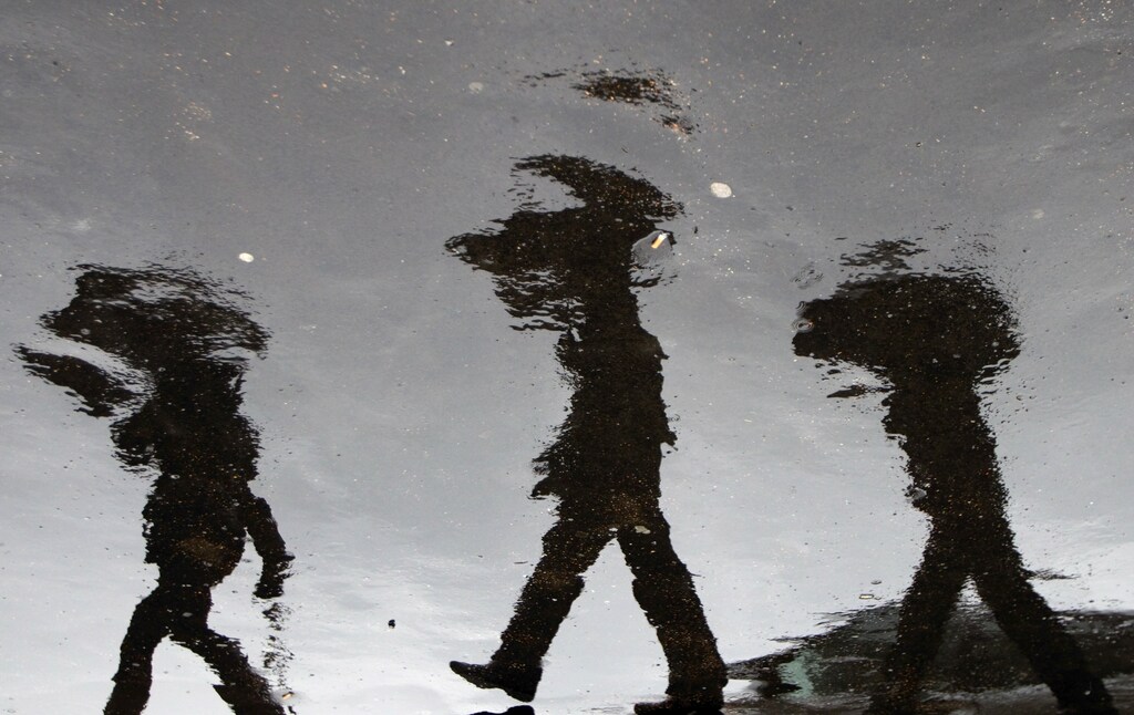 People holding umbrellas are reflected in puddles of rain at the Vatican Radio where the head of the Irish Bishops Conference Cardinal Sean Brady is leading a news conference following a two-day meeting with Pope Benedict XVI February 16, 2010. Irish bishops have promised Pope Benedict that they are committed to cooperating with civil authorities over a vast paedophilia scandal, the Vatican said on Tuesday. The picture is rotated 180-degree. REUTERS/Max Rossi (VATICAN - Tags: SOCIETY ENVIRONMENT) - GM1E62H03XA01