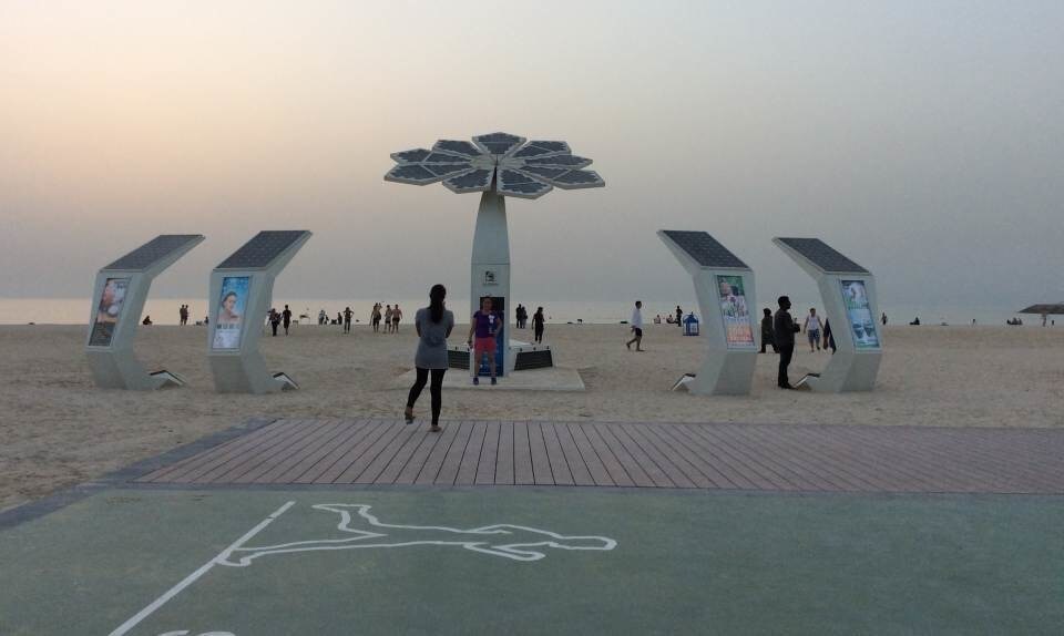 Passersbys examine a “Smart Palm” solar tree that offers phone recharging, Wi-Fi access and local information on Burj Al Arab beach in Dubai, UAE.
