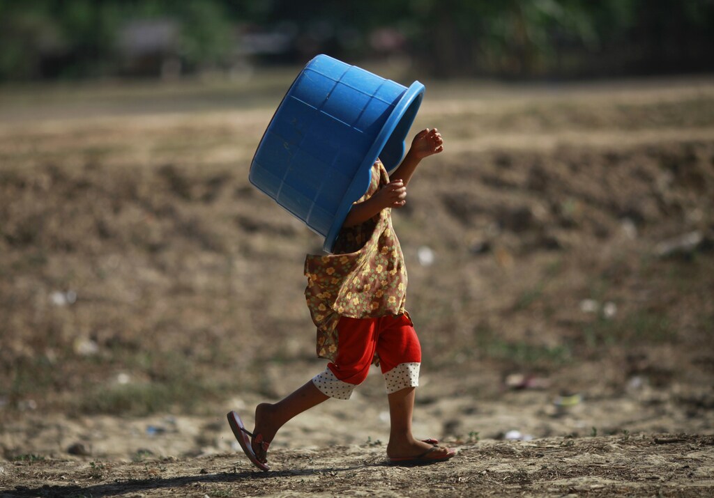A girl carries an empty bucket over her head to collect water at Yazarthingyan lake in Dala township, near Yangon May 12, 2013. Dala township is located near the sea and the only source of freshwater is from the inland lakes which have all dried up, with the exception of Yazarthingyan lake. According to the local authorities, the lake is only open to locals once every three days, with over 1,000 people lining up to collect water when the authorities open the lake from 4 pm to 5 pm. REUTERS/Soe Zeya Tun (MYANMAR - Tags: SOCIETY ENVIRONMENT TPX IMAGES OF THE DAY) - GM1E95C1MTN01