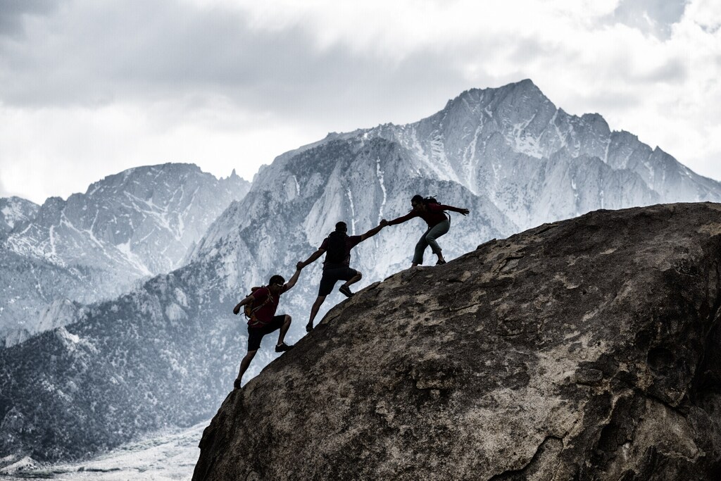 Tres amigos escalando en roca, ayudándose entre sí en un escenario dramático: La colaboración debería ser un rasgo clave de liderazgo