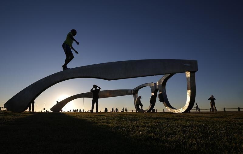 Youths pose for photographs as they climb on top of a sculpture in the form of a giant pair of spectacles on Cape Town's Sea Point Promenade, November 18, 2014. Inspired by Nelson Mandela, the work 'Perceiving Freedom' by artist Michael Elion has stirred some controversy in the local media. While popular with visitors to the promenade, some critics have questioned the association of Mandela's legacy with commercial sponsors.