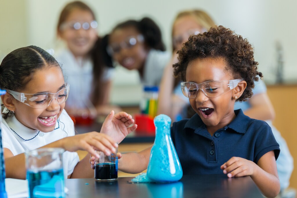 Diverse private school classmates are excited as foam overflows from beaker during chemistry experiment, symbolizing behavioural experiments.