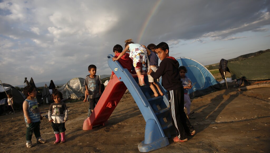 Children play on a slide as a rainbow forms overhead at a makeshift camp for refugees and migrants at the Greek-Macedonian border near the village of Idomeni, Greece, May 22, 2016.