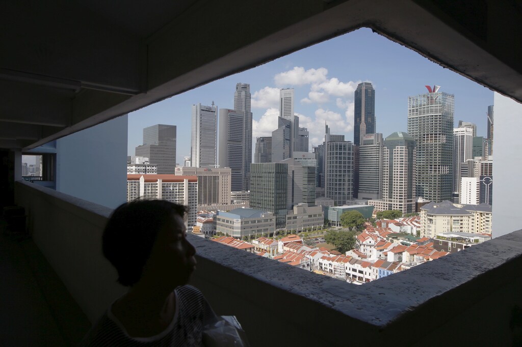A woman passes the skyline of the central business district, in a public housing estate in Singapore, April 14, 2015. Singapore's central bank on Tuesday surprised markets by holding them off from further monetary easing, saying an improved outlook for global growth would underpin the trade-reliant economy