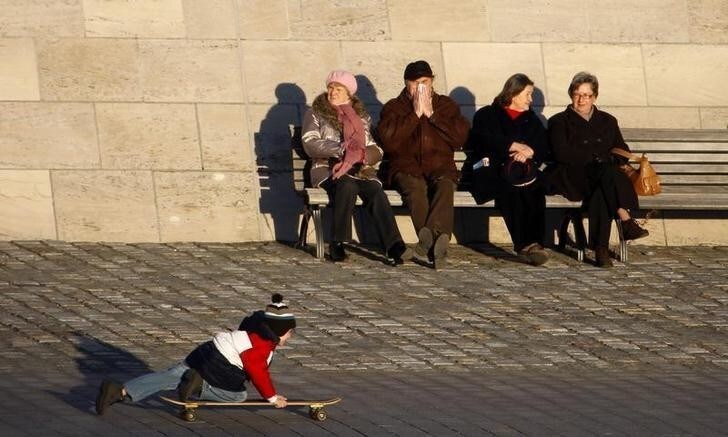 A boy enjoys the sun on a skateboard while elderly people sit on a bench in Berlin January 13, 2008. REUTERS/Johannes Eisele (GERMANY)
