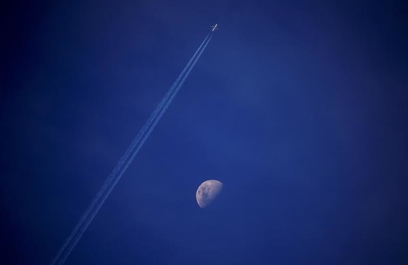 A plane leaves a vapor trail as it flies past the moon above the town of Gunnedah, New South Wales, Australia July 21, 2018. Picture taken July 21, 2018.