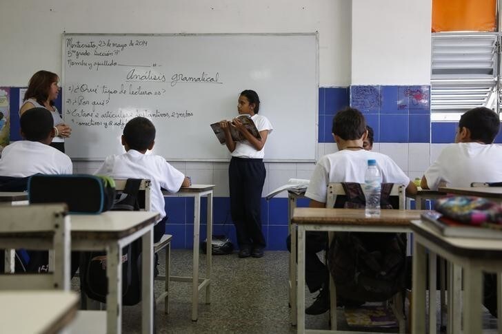 A girl reads a state-issued textbook from the "Bicentennial Collection" in front of her classmates at a classroom of the Eleazar Lopez Contreras school in Caracas May 23, 2014. Venezuela's government has published dozens of new textbooks that glorify late president Hugo Chavez and belittle his adversaries, infuriating opposition critics who call them part of a campaign to indoctrinate school children. Originally introduced in mid-2011, the textbooks have become a hot-button issue again amid a broad state-run review of the education system that some fear could boost the ruling Socialist Party's imprint on classrooms. Picture taken on May 23, 2014. REUTERS/Carlos Garcia Rawlins (VENEZUELA - Tags: EDUCATION POLITICS)