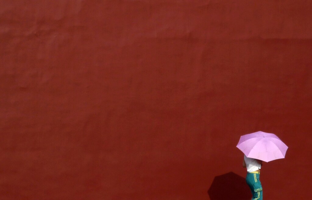 A woman uses an umbrella to shade herself from the sun as she walks next to a wall surrounding the Forbidden City in central Beijing August 27, 2009. REUTERS/David Gray (CHINA SOCIETY ENVIRONMENT) - GM1E58R10OH01